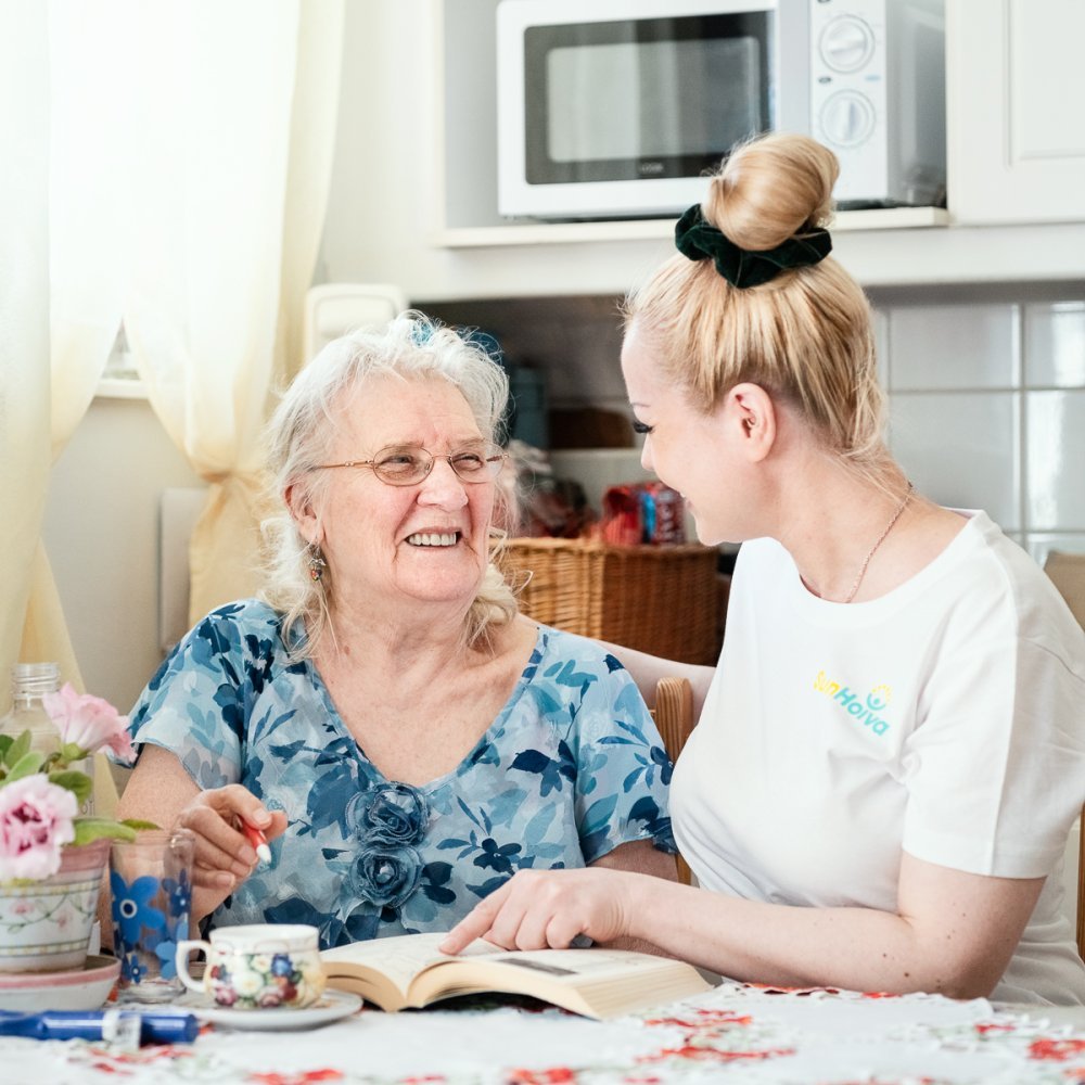 Kotihoidon asiakas ja hoitaja nauravat pöydän ääressä